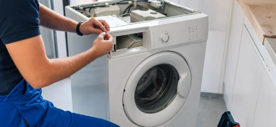 Técnico abriendo una lavadora en una cocina para diagnosticar la avería antes de decidir si se repara o se lleva al punto limpio